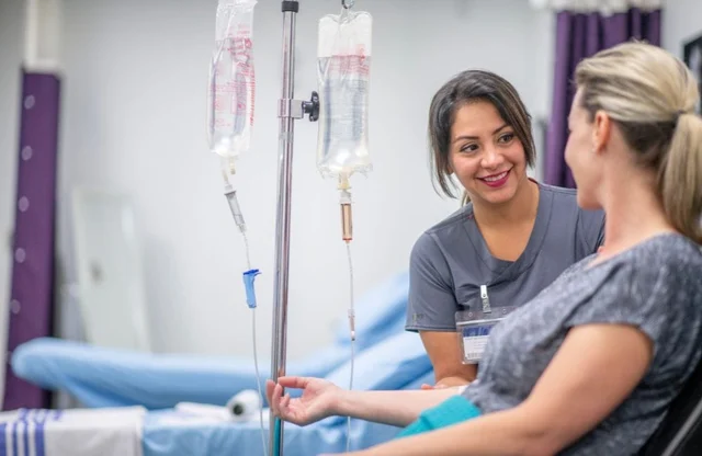 An IV drip being administered to a woman in a medical setting, with a healthcare professional smilin.