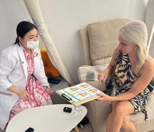 A woman in a pink patterned dress and face mask consulting with a healthcare professional holding a.