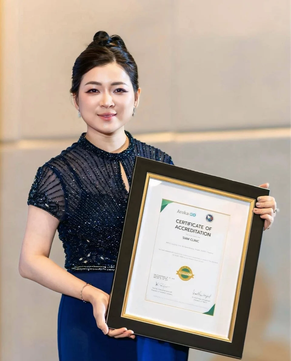 Certificate of accreditation held by a woman in a dark blue dress, smiling, at an award event.