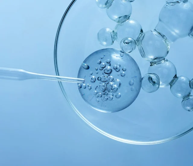 A clear glass petri dish with a pipette and several glass beads or spheres, all in a blue-tinted set.