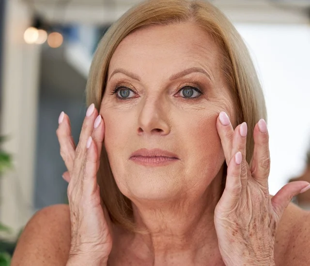 A woman with blonde hair applying skincare around her eyes.