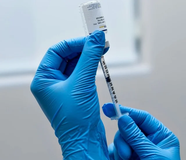 A healthcare professional's gloved hands preparing a syringe with a vial for injection.