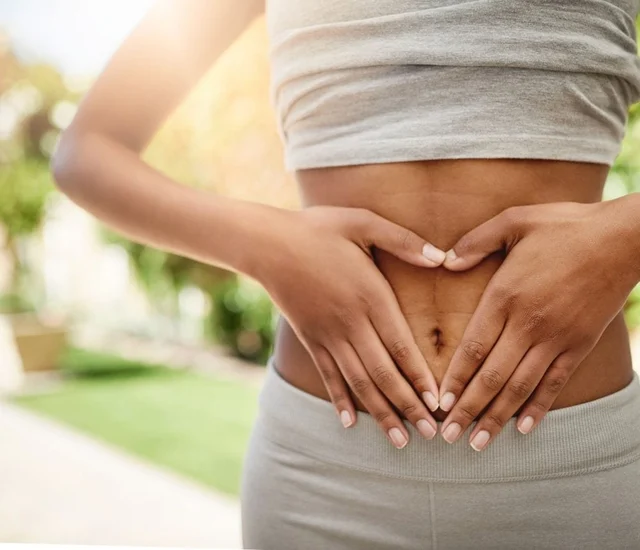 Woman holding her stomach with both hands, forming a heart shape outdoors.