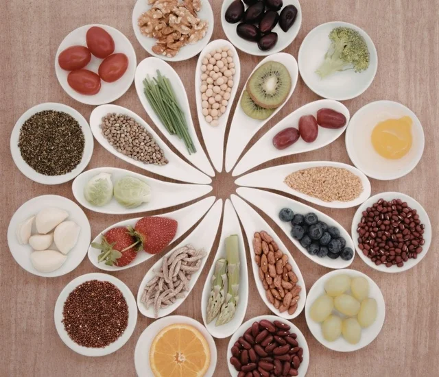 Fresh fruits, vegetables, nuts, seeds, and legumes arranged in small white dishes on a wooden surfac.