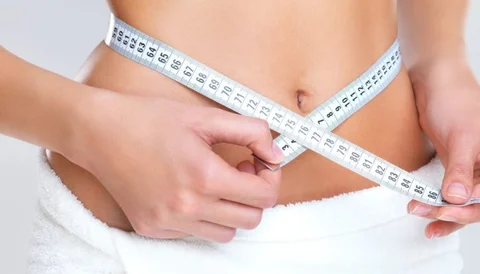 A woman measuring her waist with a tape measure, focusing on abdominal area.