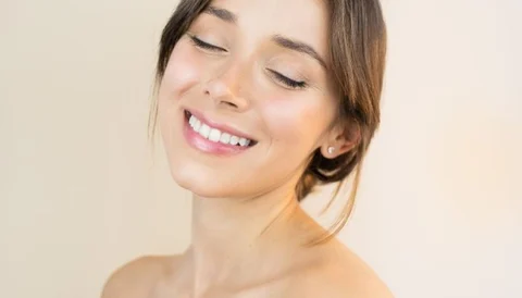 A smiling woman with clear skin and closed eyes, facing slightly to the right.