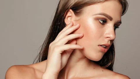 A young woman with smooth skin touching her face, showcasing facial contours.