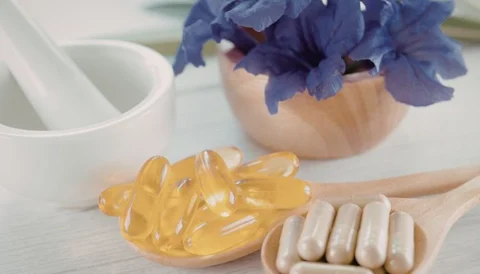 Omega-3 capsules and supplements on wooden spoons with a blue flower in the background.