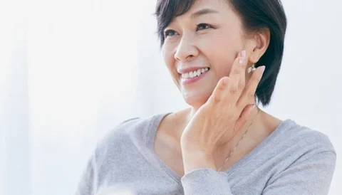 A smiling woman touching her face, demonstrating facial rejuvenation.