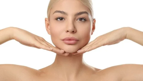 A young woman with clear skin and blonde hair, holding her face with both hands.