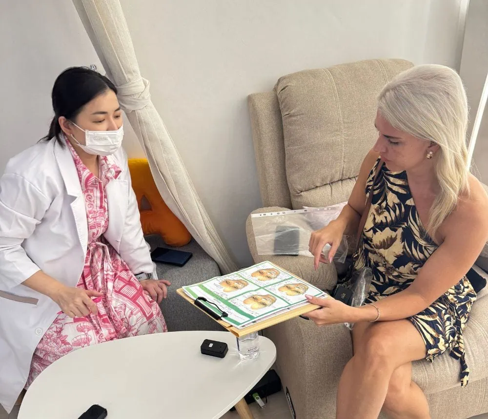 A woman in a pink patterned dress and face mask consulting with a healthcare professional holding a.