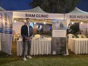A man standing in front of a Siam Clinic booth at an outdoor event during evening.