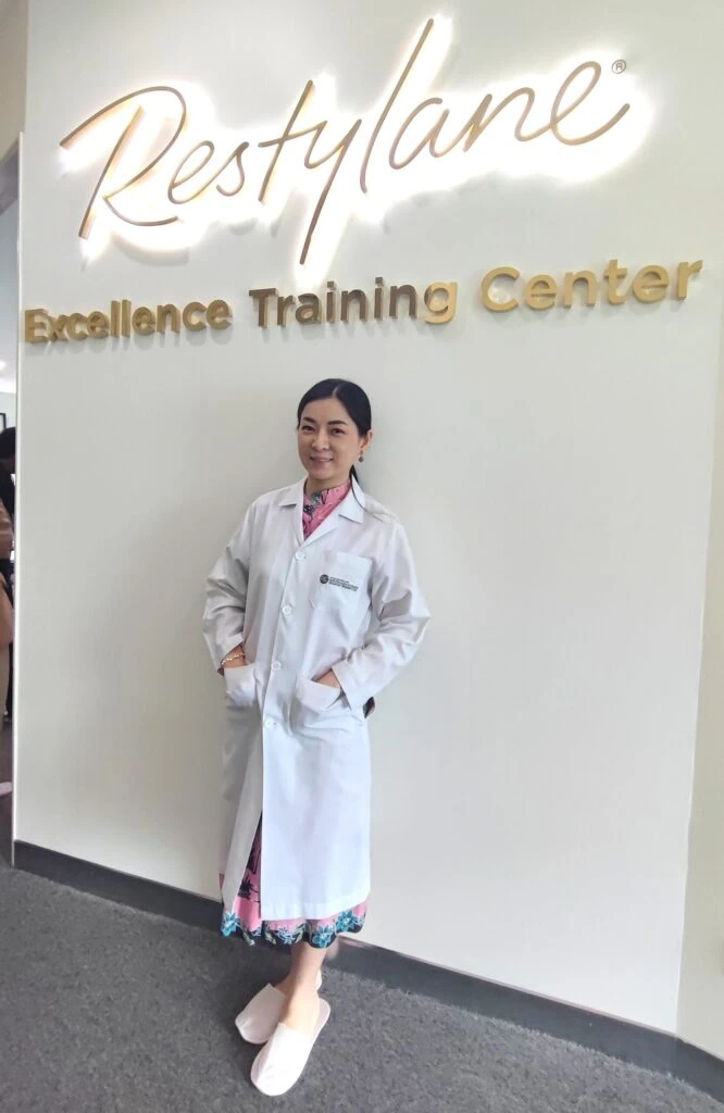 A healthcare professional standing in front of a wall with "Restylane Excellence Training Center" si.