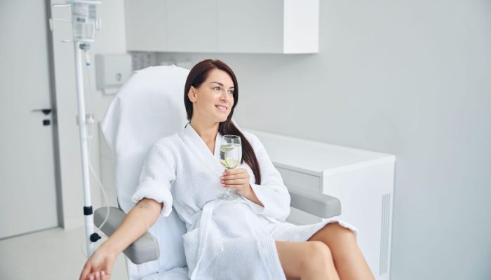 A woman relaxing in a medical chair with an IV drip, holding a glass of water.