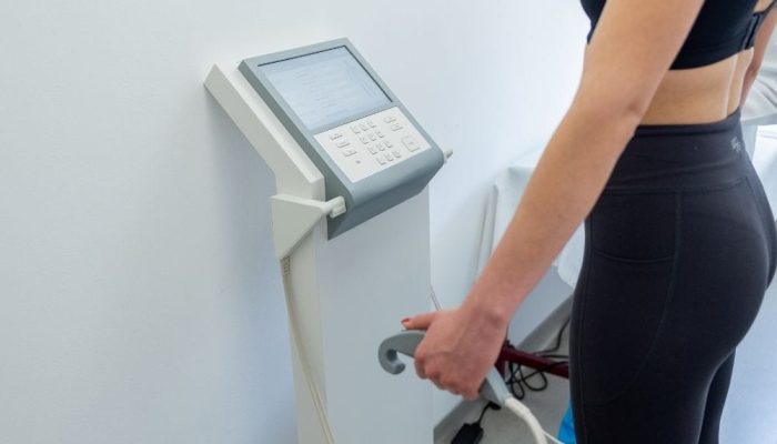 A woman in black athletic wear using a body composition analyzer machine.
