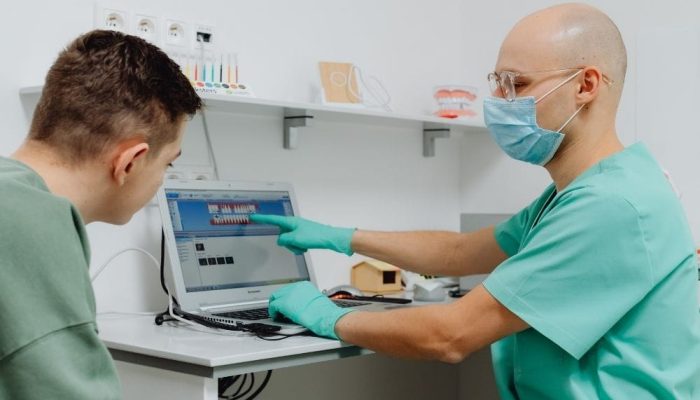 A healthcare professional explains test results to a patient using a laptop in a medical office.