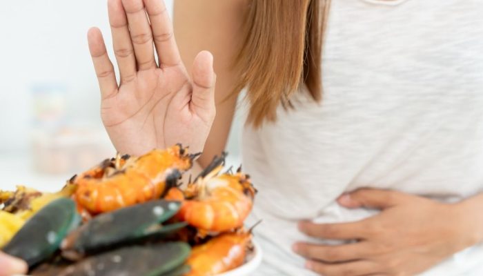 Allergy test sample with seafood and vegetables, woman holding hand up to avoid food, digestive heal.
