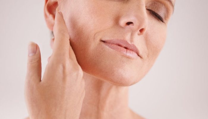 A woman with clear skin gently touching her jawline, eyes closed, relaxed expression.