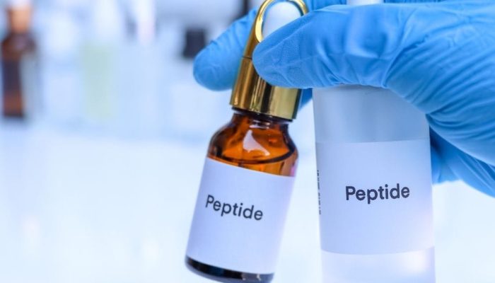 A vial labeled "Peptide" held by a gloved hand in a laboratory setting.
