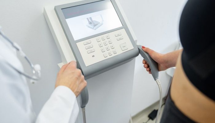 A woman holding a handheld device connected to a body composition analyzer machine.
