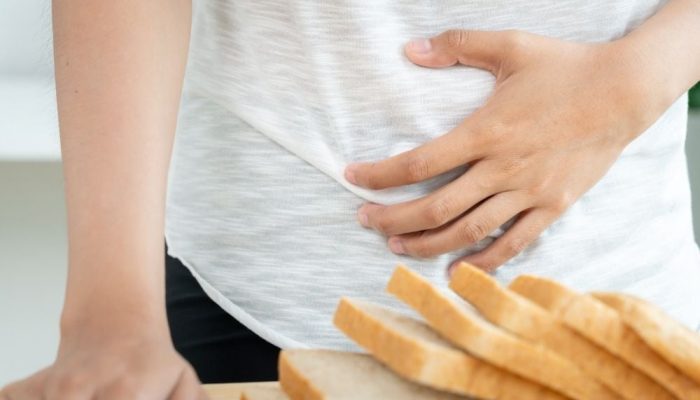 A woman holding her stomach, with sliced bread on a table in front of her.