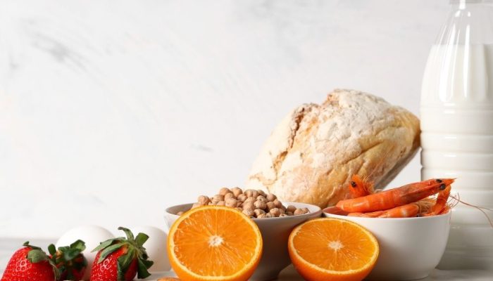 A healthy breakfast with bread, orange, shrimp, nuts, and a bottle of milk on a white surface.