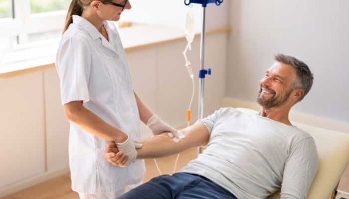 A healthcare professional preparing to draw blood from a smiling man in a medical clinic.